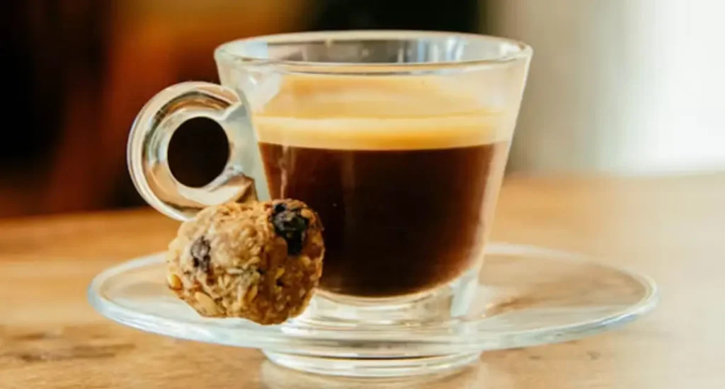 Lungo vs Espresso Explained: What’s the Difference? 5 A freshly brewed lungo coffee in a small espresso cup with a layer of crema on top, served on a wooden table.