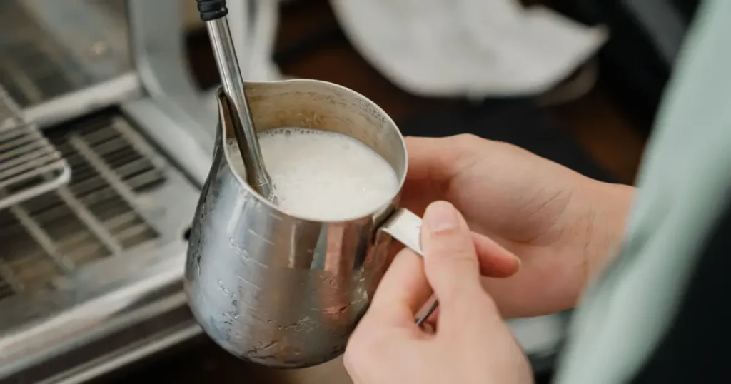 Common Nespresso Problems & Fixes (2026 Guide) 4 Barista frothing milk with a steam wand to create smooth microfoam, illustrating milk frother troubleshooting and proper milk texturing.