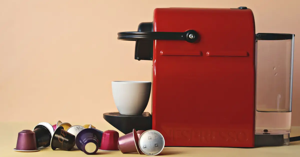 Nespresso Vertuo Capsules Ranked (2026) 2 Red Nespresso Vertuo machine brewing coffee with Vertuo capsules displayed beside it